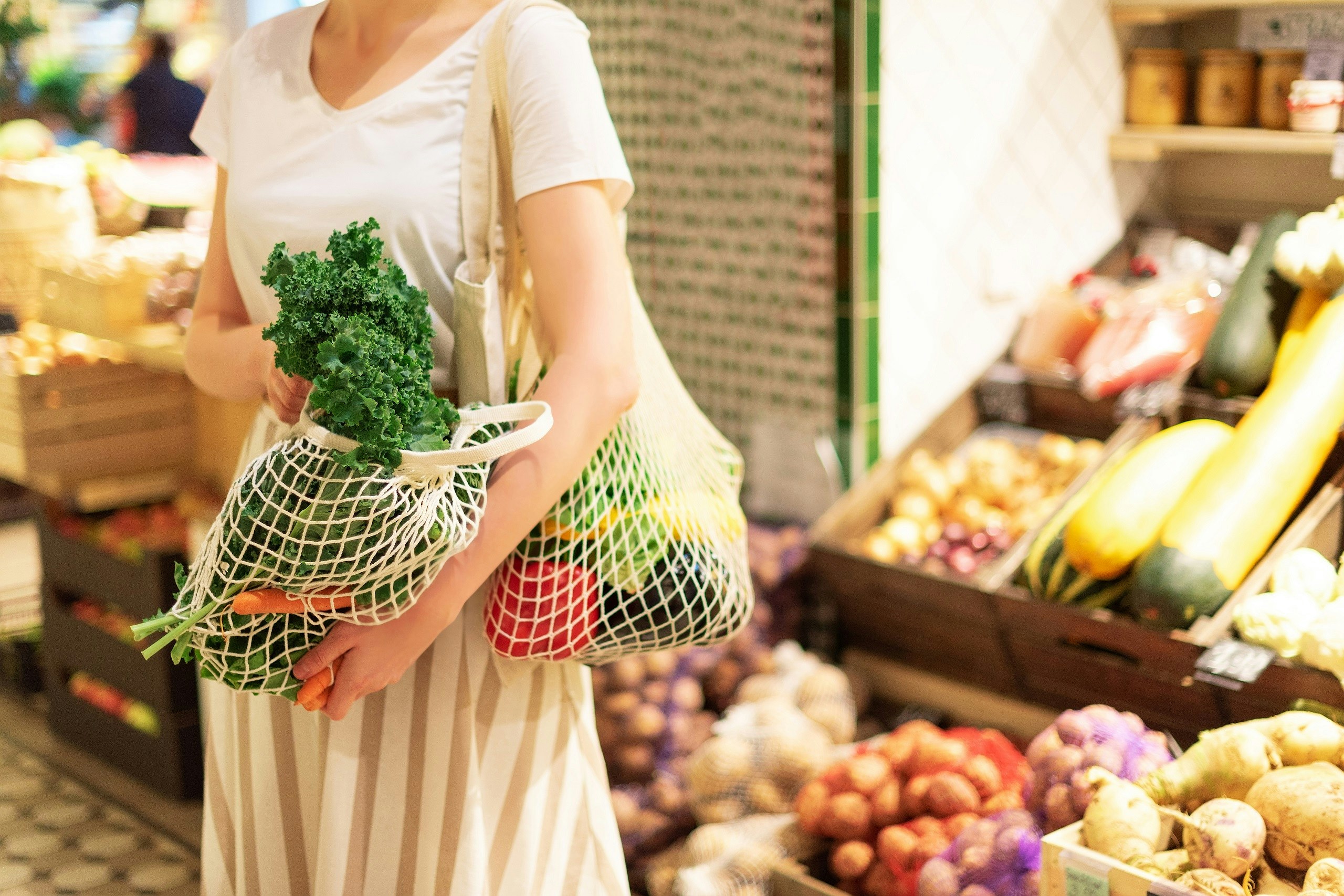 Frau im Supermarkt beim Einkauf. Sie ist in der Obst-und Gemüse Abteilung und hat auch schon einige Einkäufe in umweltfreundlichen Gemüsenetzen über der Schulter hängen.
